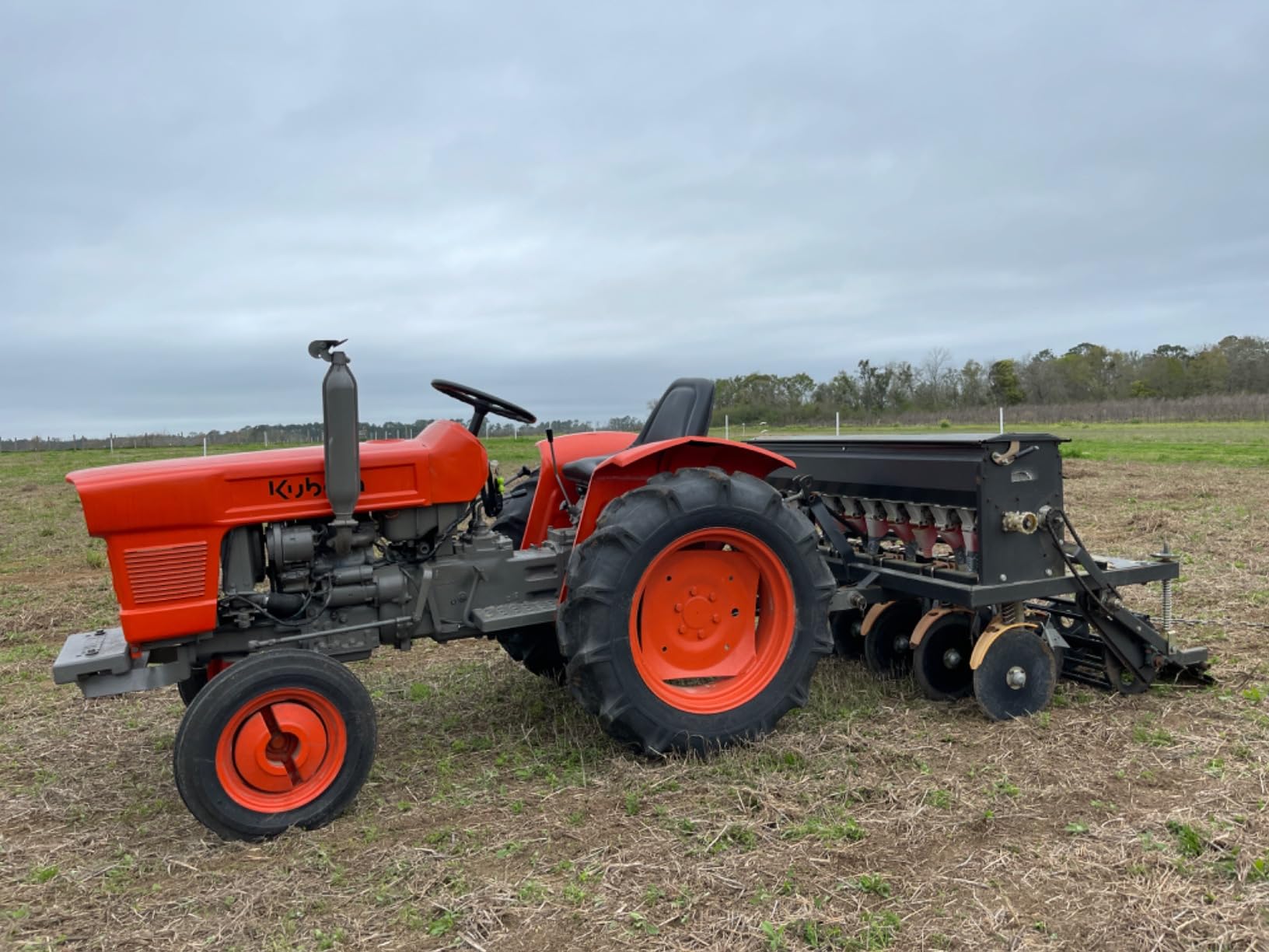 Side view of a Field Tuff seeder on a Kubota tractor showing the coulters and hopper