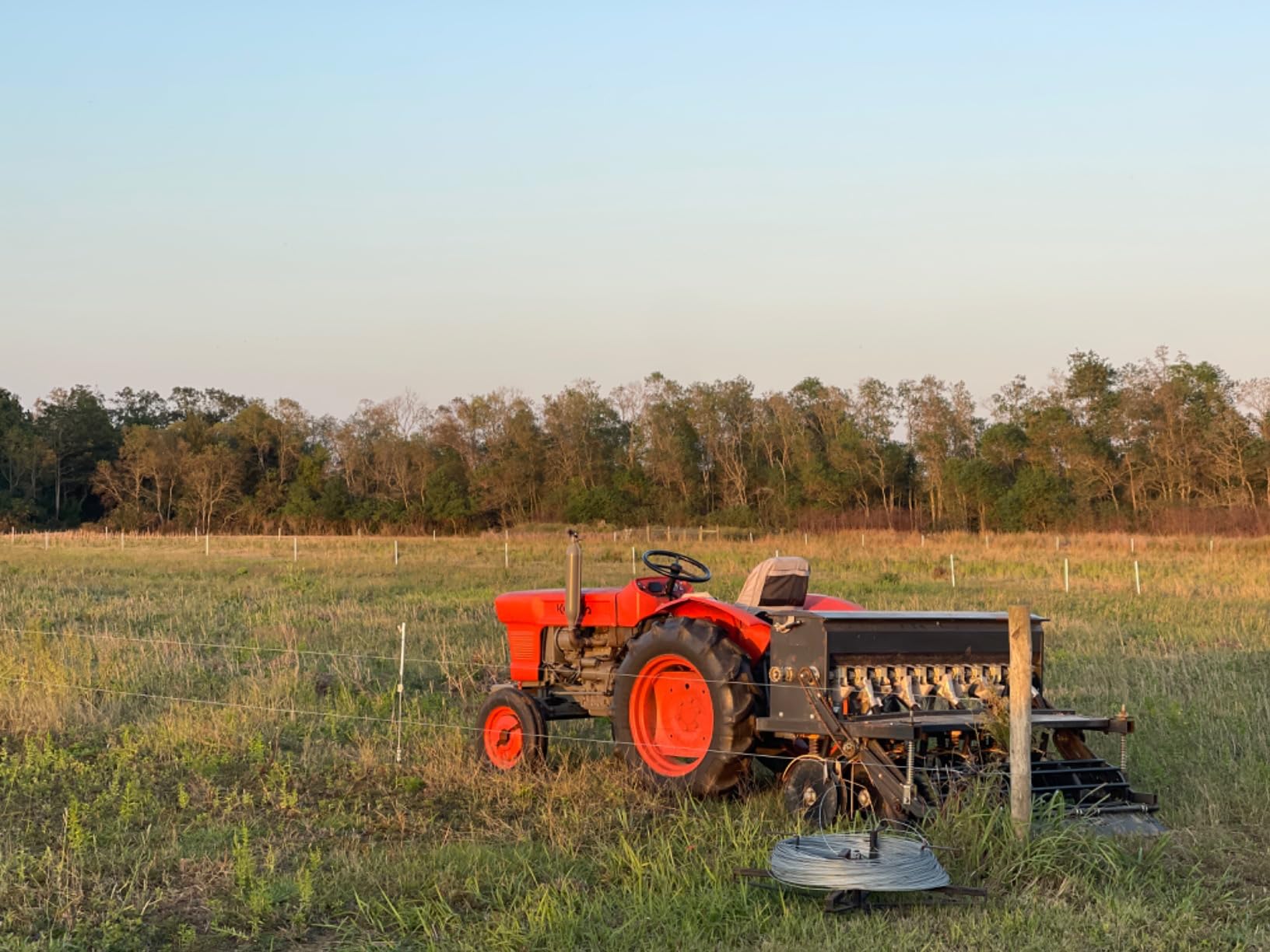Kubota tractor and Field Tuff seeder parked at sunset beside a wire fence line