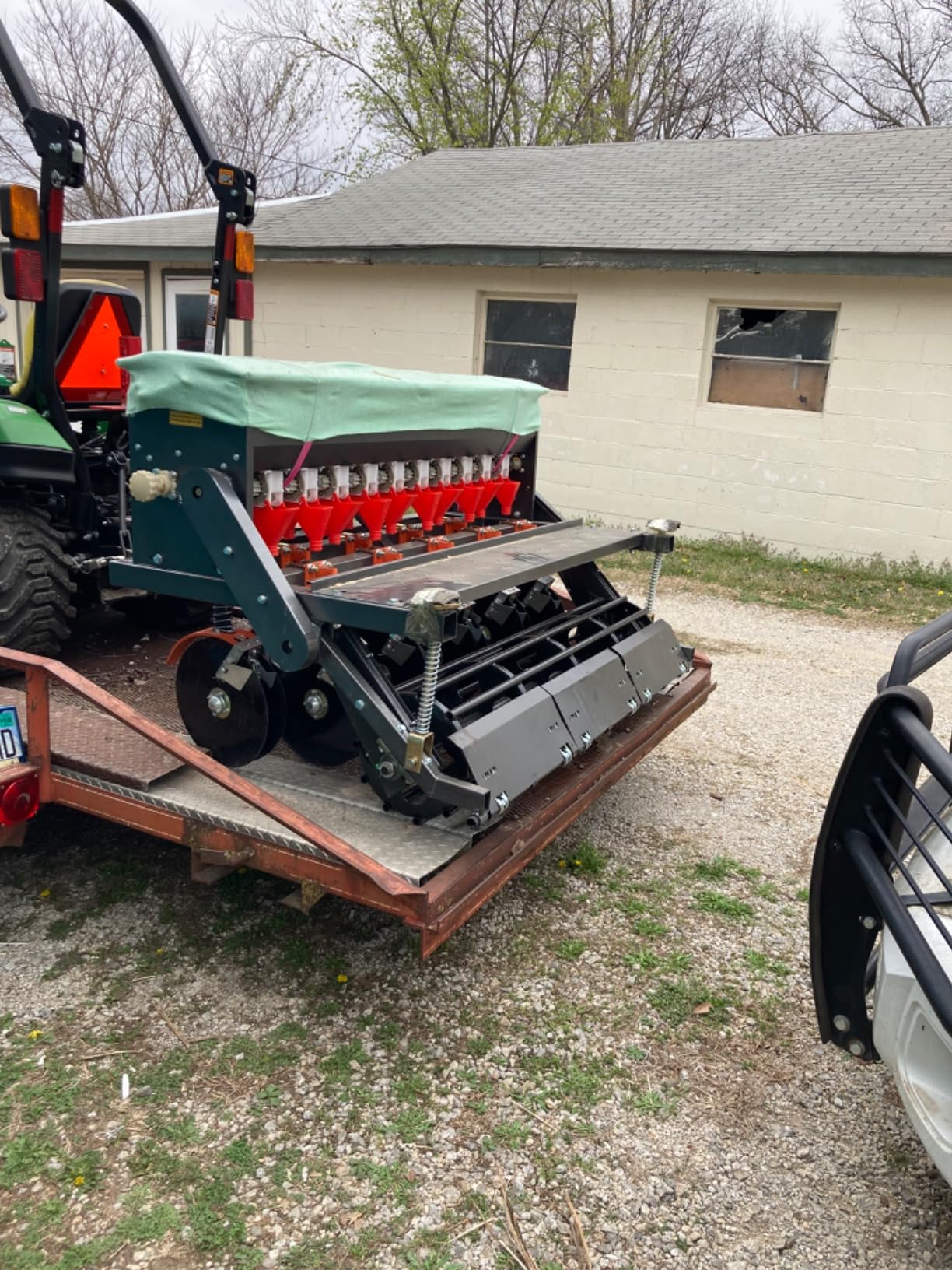Field Tuff seeder with covering discs loaded on a trailer behind a John Deere tractor