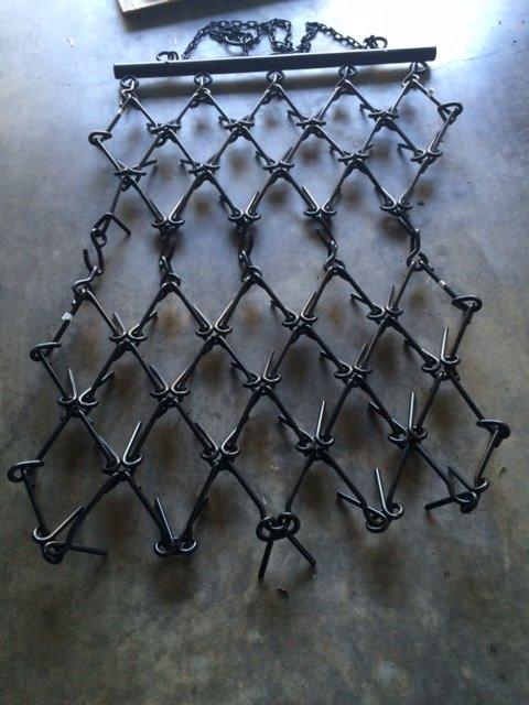 Field Tuff chain drag harrow laid flat on a concrete floor with the tow bar attached