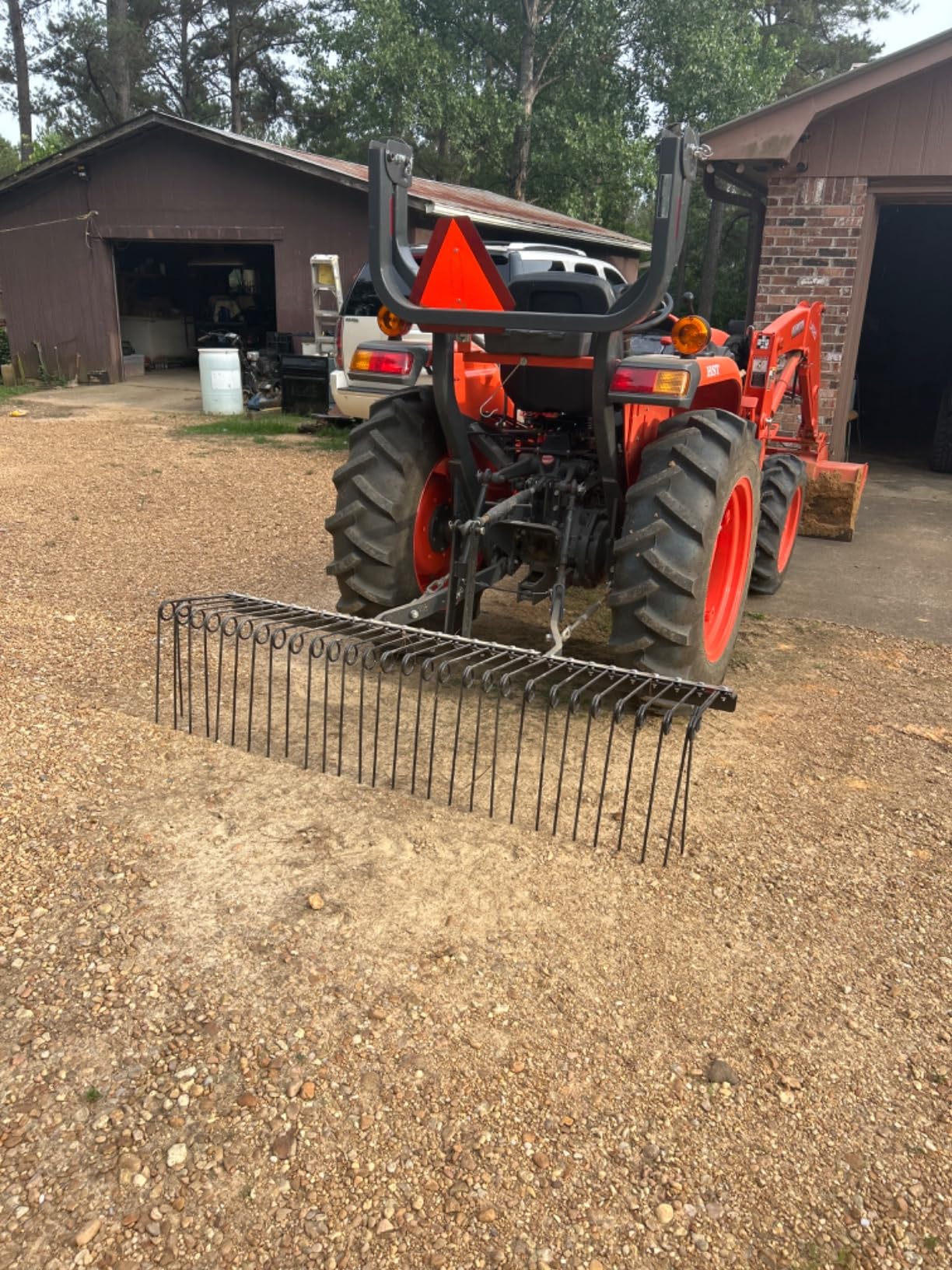 Field Tuff 3-point spring tine rake behind a Kubota tractor with a front loader on a gravel drive